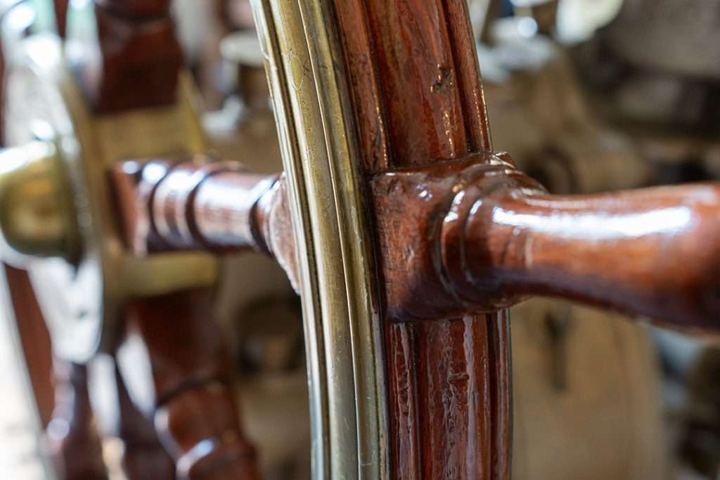 Close-up of a polished wooden ship’s wheel aboard HMS Wellington