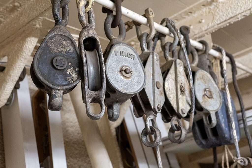 Vintage metal pulleys and rope blocks hanging aboard HMS Wellington, part of the ship’s rigging