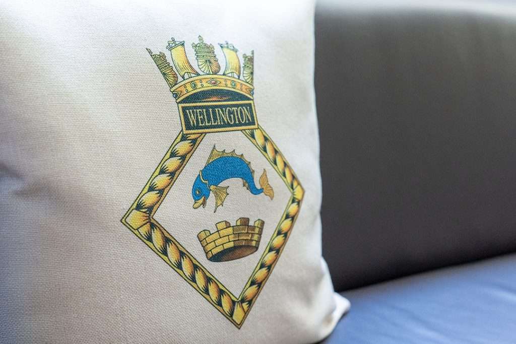 Cushion featuring the HMS Wellington crest with a crown, dolphin and castle placed on a seat on board the ship